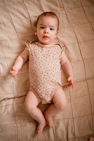 Baby wearing polka dot onesie lying on quilted beige bedding.