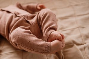 Close-up detail of baby feet in soft pink knitted clothing against cream bedding.