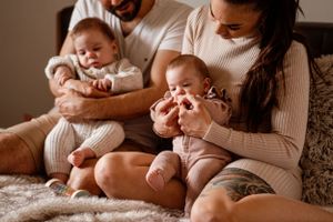 Warm-toned photo of family relaxing together with their babies on cozy bedding.