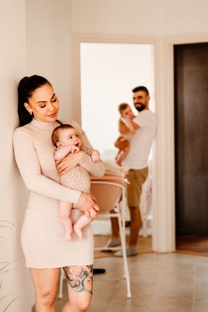 Modern family portrait in neutral tones with mother holding baby in foreground of bright room.