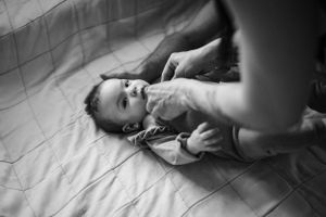 Black and white photo of a baby lying on bed while being cared for.