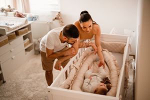 Parents leaning over white crib looking lovingly at their baby.