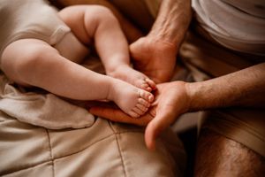 Close-up of tiny baby feet being gently held by adult hands on beige bedding.