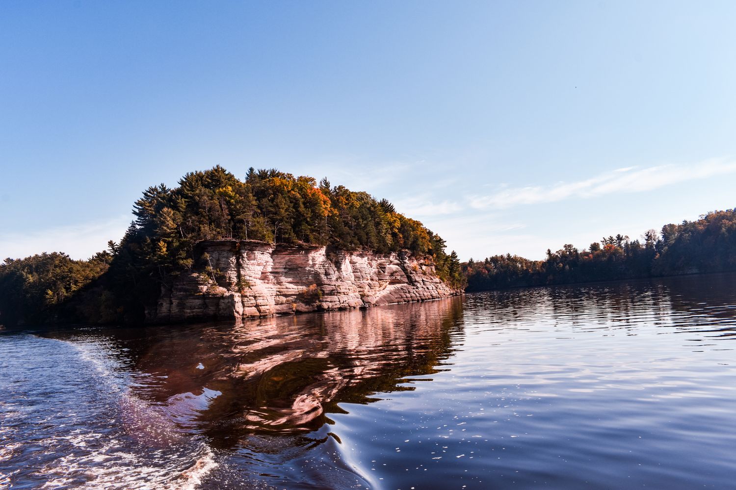 Scenic limestone cliffs reflect in calm lake waters during golden hour.