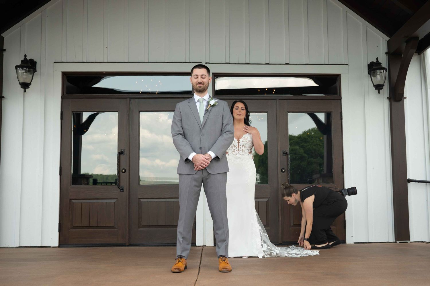 A photographer adjusts a wedding dress train in front of a white venue entrance.