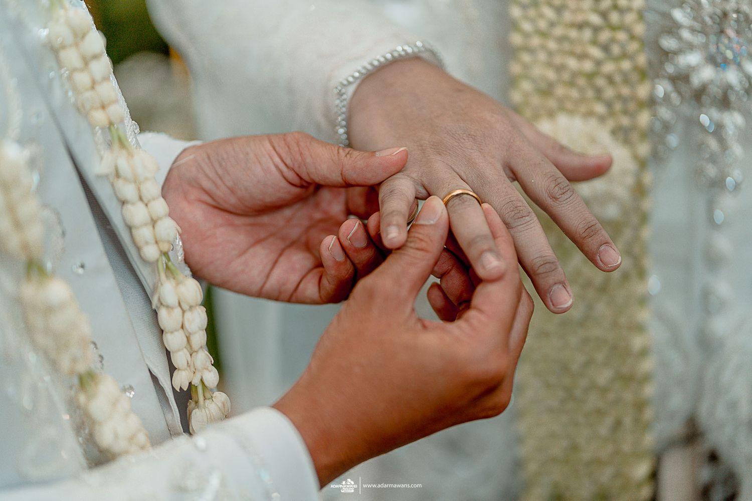 Close-up of hands during traditional ring exchange ceremony with white attire details.
