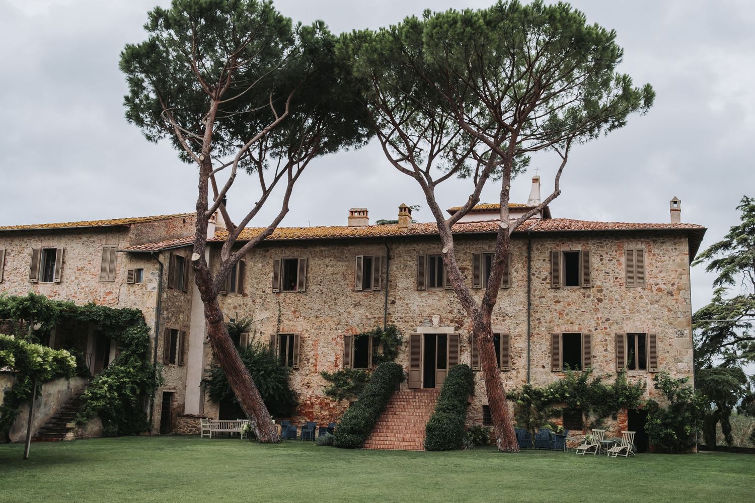 Panoramic view of a rustic Tuscan villa with stone walls and cypress trees.