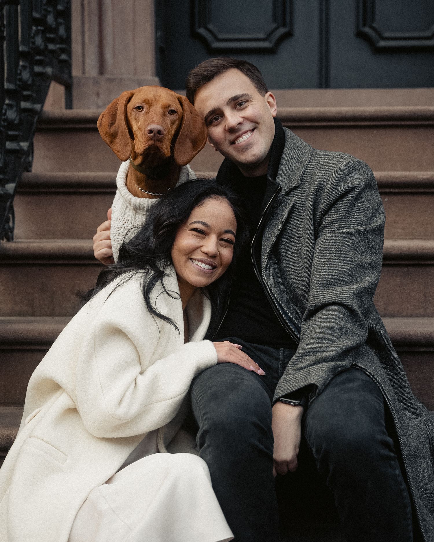 An engaged couple shares joyful moments with their dog on urban steps.