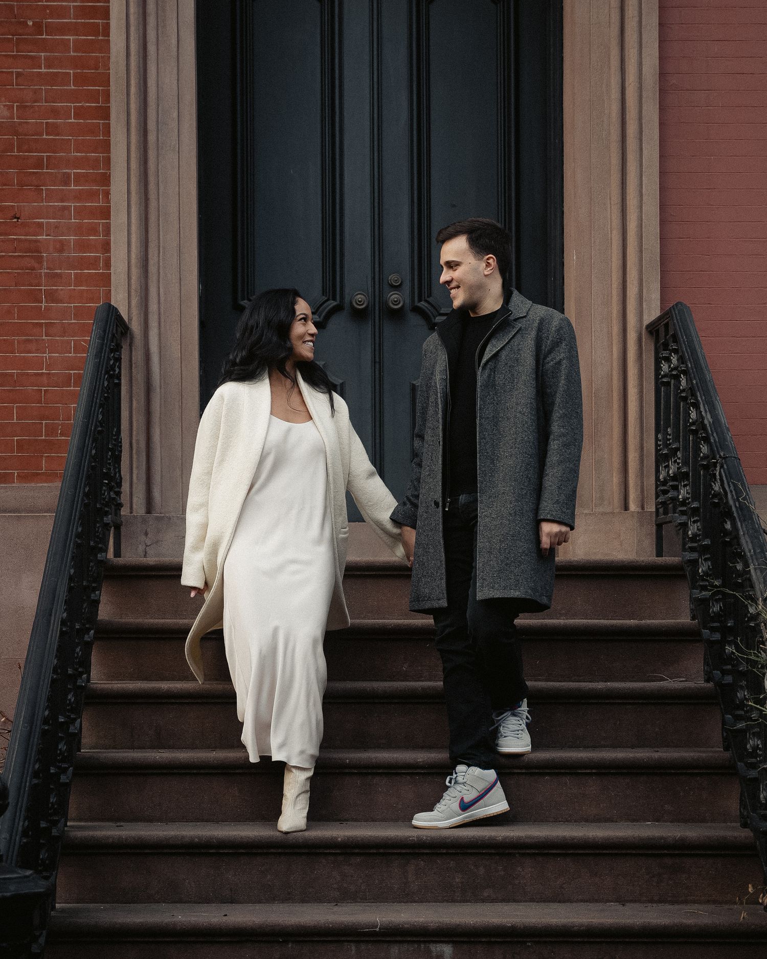 A couple in contrasting black and white outfits poses on brownstone steps.
