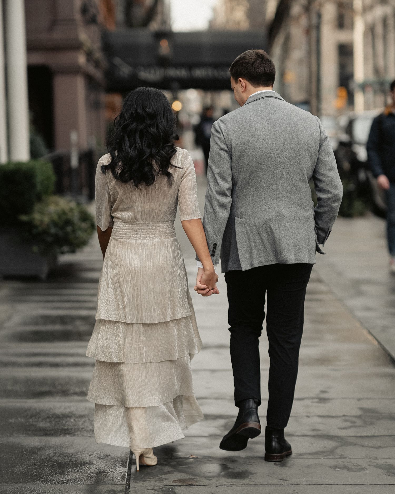 A couple walking hand in hand down a rainy city sidewalk.