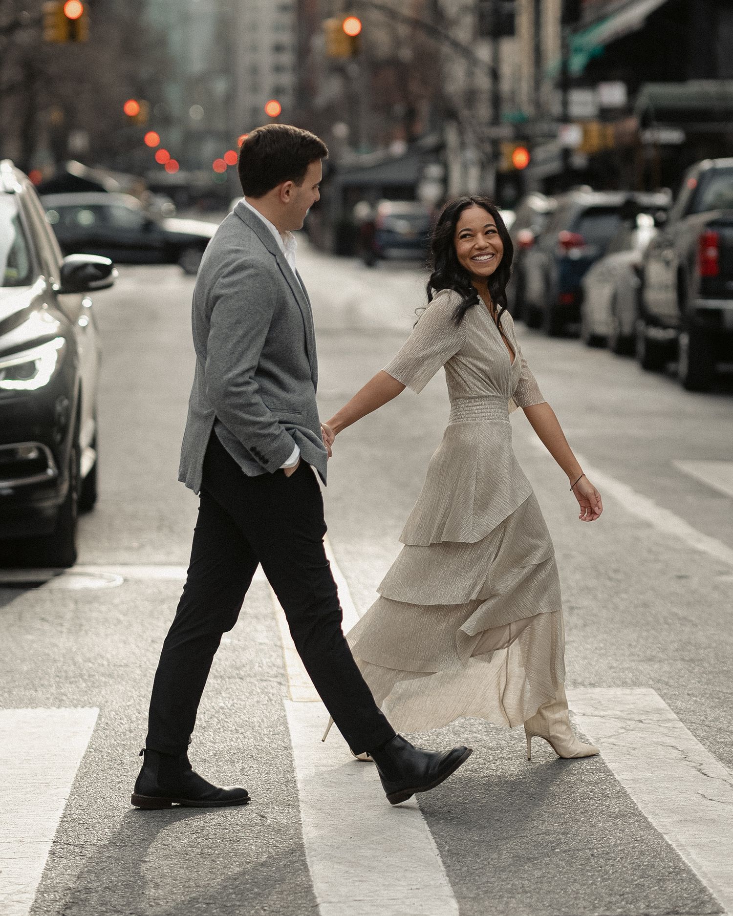 A couple walking across a city crosswalk, her dress flowing in an elegant motion.