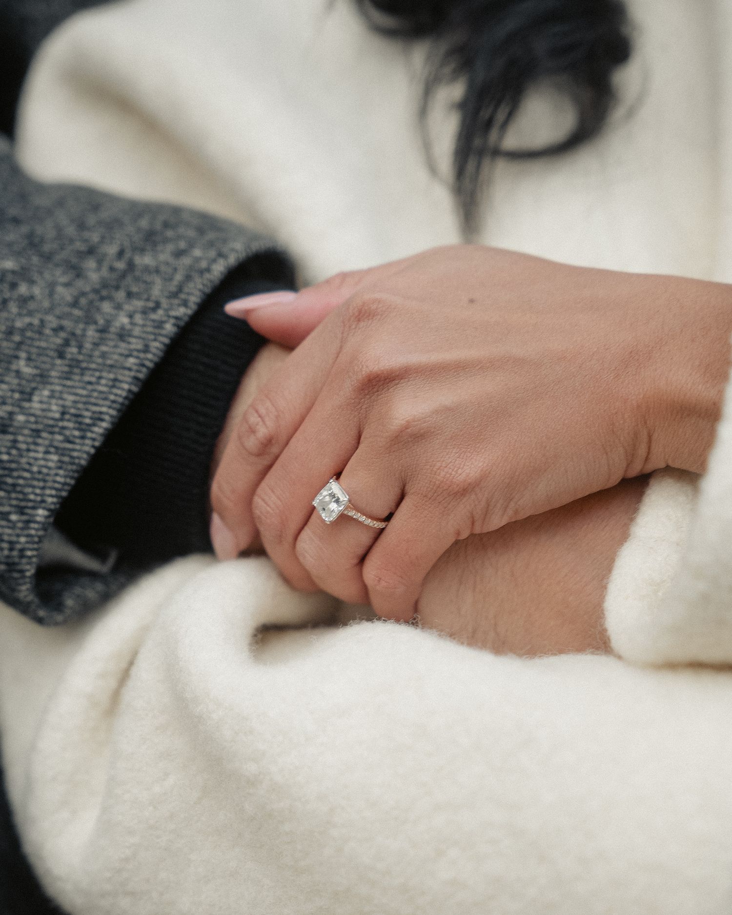 Close-up shot of hands showing off an engagement ring against a white sweater.
