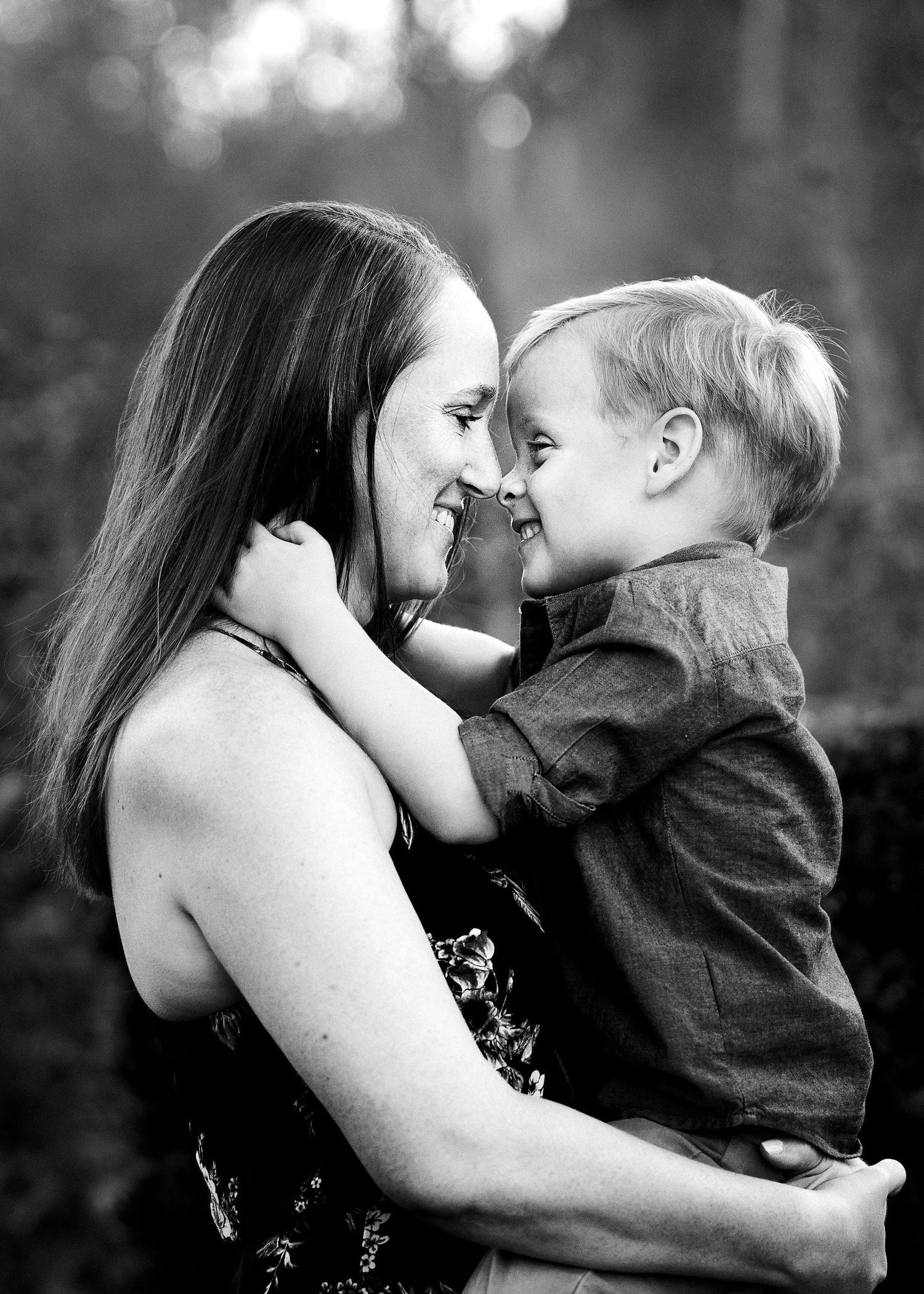 a black and white portrait of a mother holding her preschool age son close while they touch noses