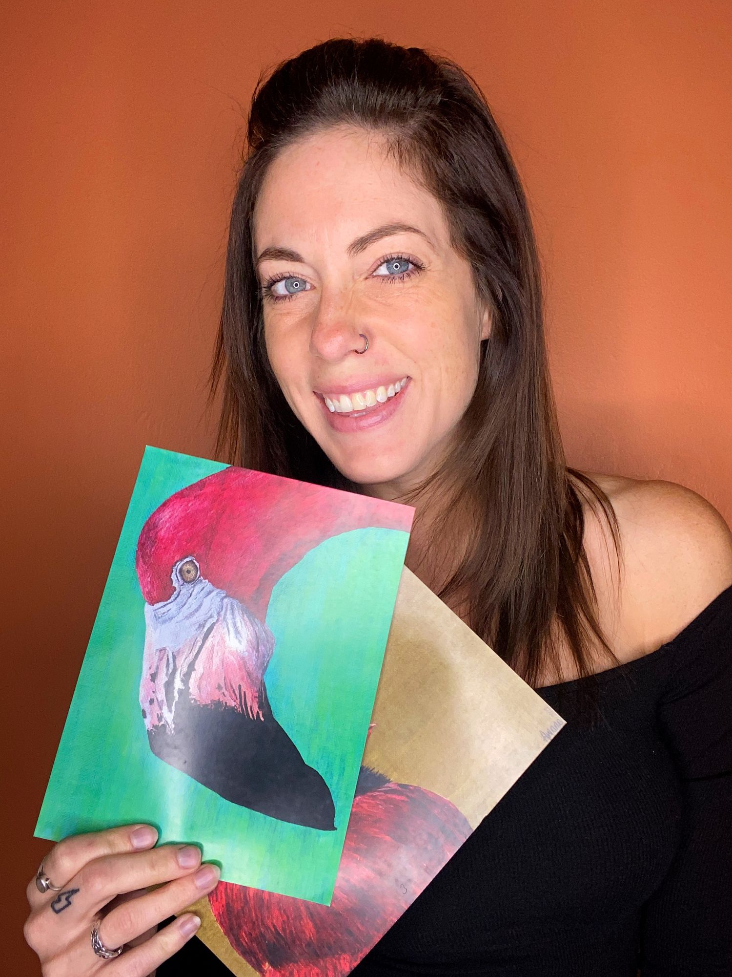 A person displaying colorful artwork prints against an orange background.