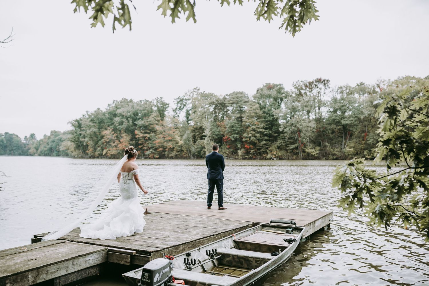 Wedding couple sharing playful moment on lakeside dock with boat.