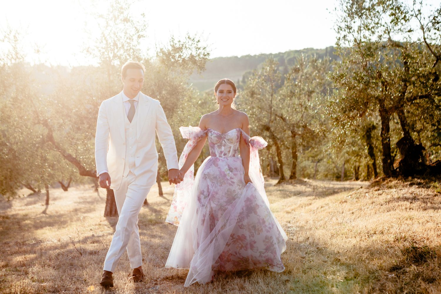 bride and groom walk hand in hand together in an olive grove at sunset