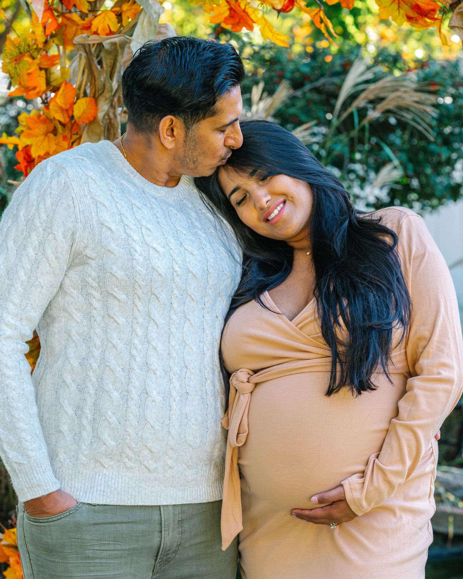 Couple in cozy sweaters share intimate moment against backdrop of fall leaves.