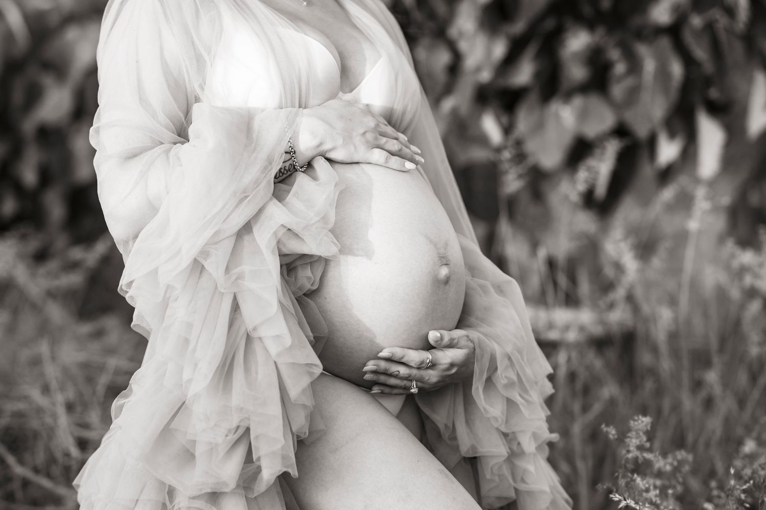 A black and white maternity photo featuring flowing sheer fabric and a pregnant belly.