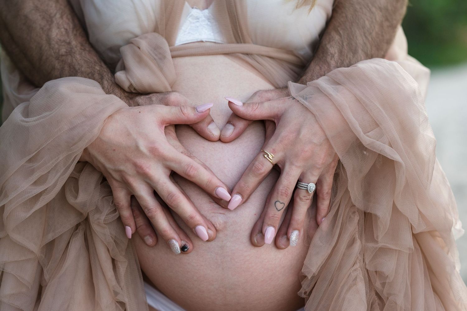 Hands form a heart shape over a pregnant belly in a flowing tulle dress.