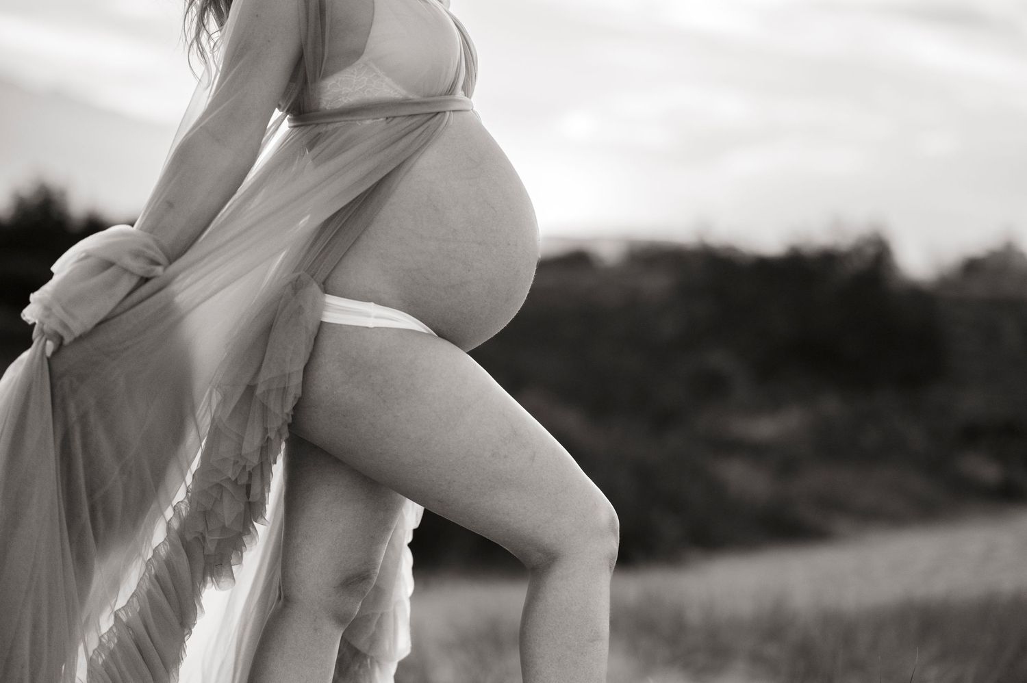 Side view silhouette of a pregnant belly in black and white with soft fabric details.