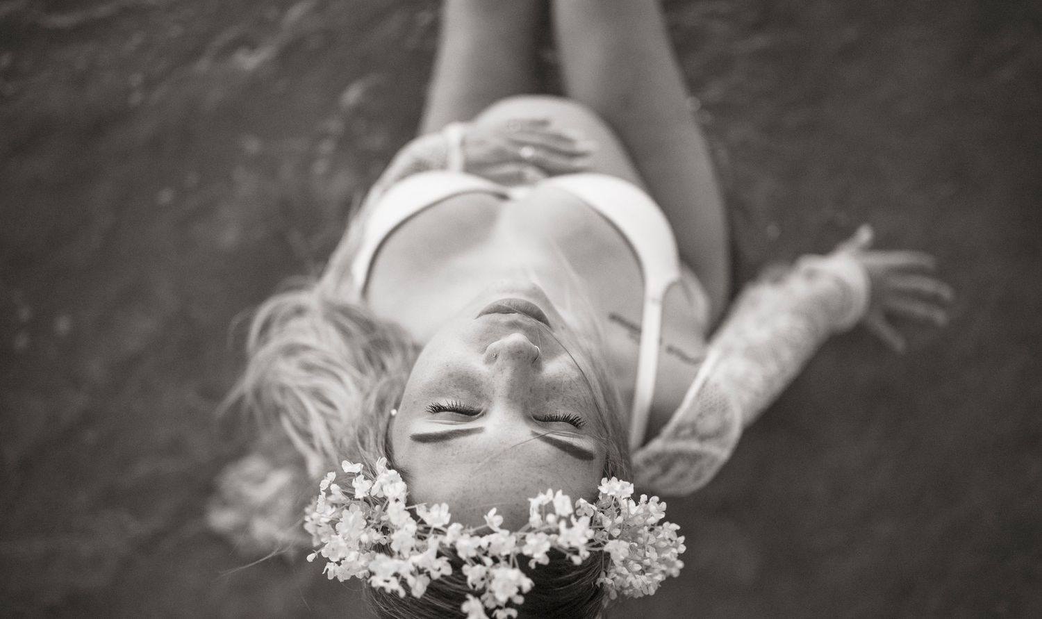 Woman lying with flower crown in artistic black and white portrait.
