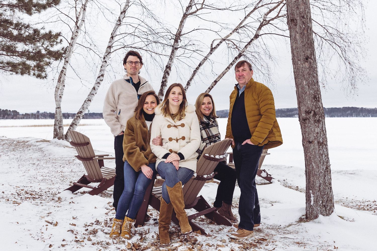 A group poses together for a winter portrait in the snow near birch trees.