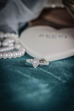 Diamond engagement ring and pearl necklace on teal velvet surface.