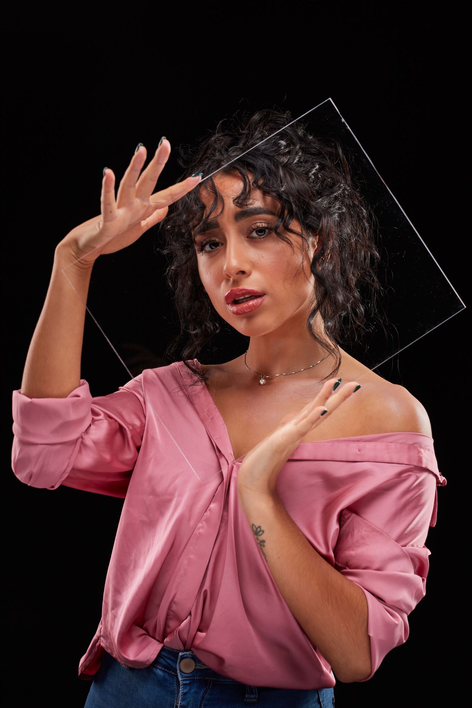 Woman in pink blouse poses with hand up against black background with transparent panel.