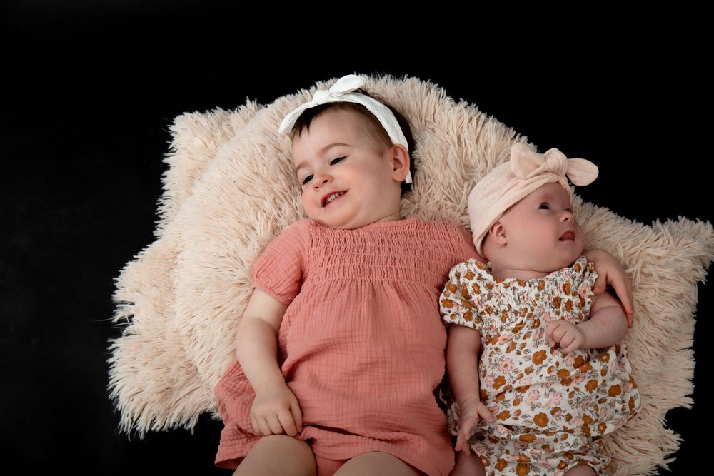 Two young children in coral and floral outfits resting on fluffy beige backdrop.