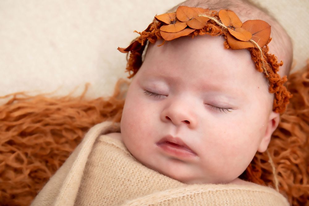 Peaceful sleeping infant wearing rust-colored headband against orange textured background.