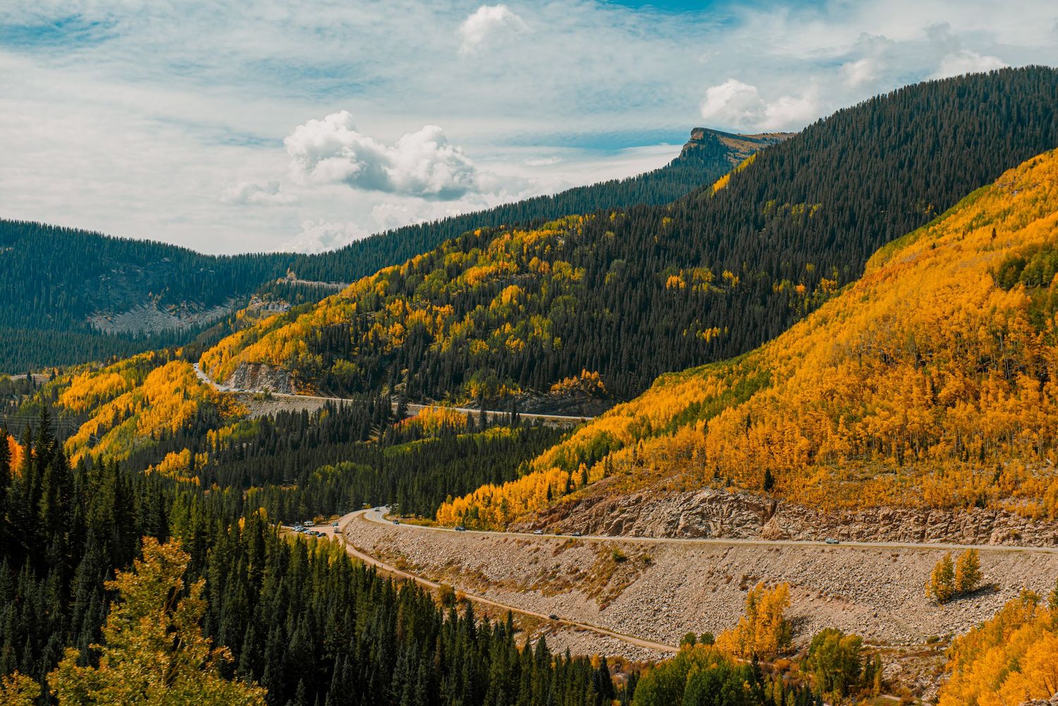 Scenic mountain landscape with golden aspens and winding road through valley.