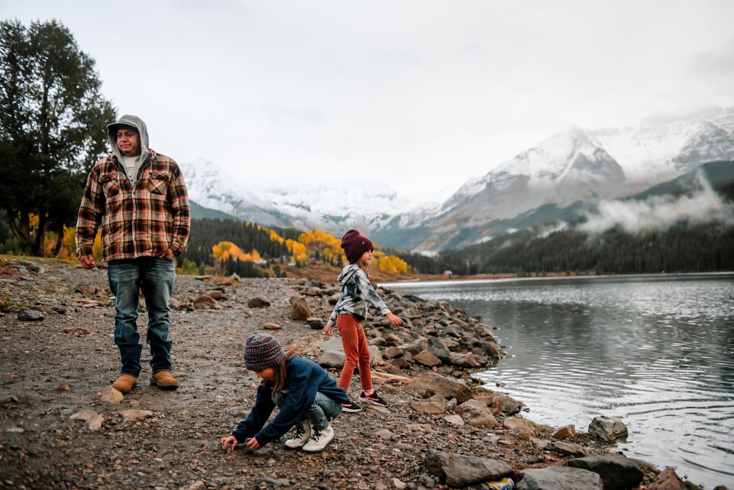 Group enjoying a casual gathering by a scenic mountain lake with snow-capped peaks in the distance.