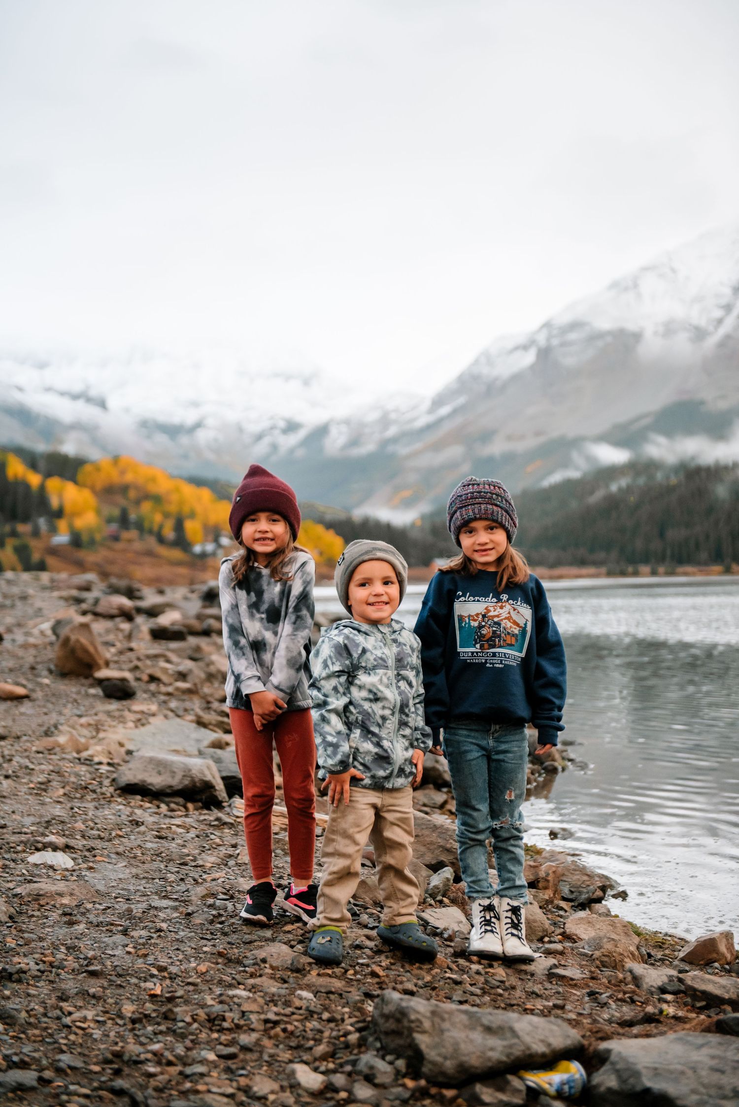 Small group exploring a rocky shoreline against a backdrop of mountains and autumn trees.