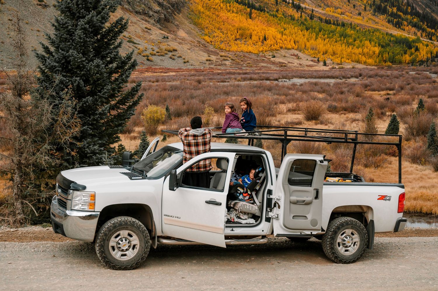 White pickup truck parked on mountain road with doors open during autumn season.