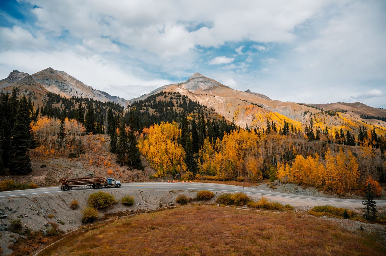 Mountain landscape with winding road and golden aspen trees against blue sky.