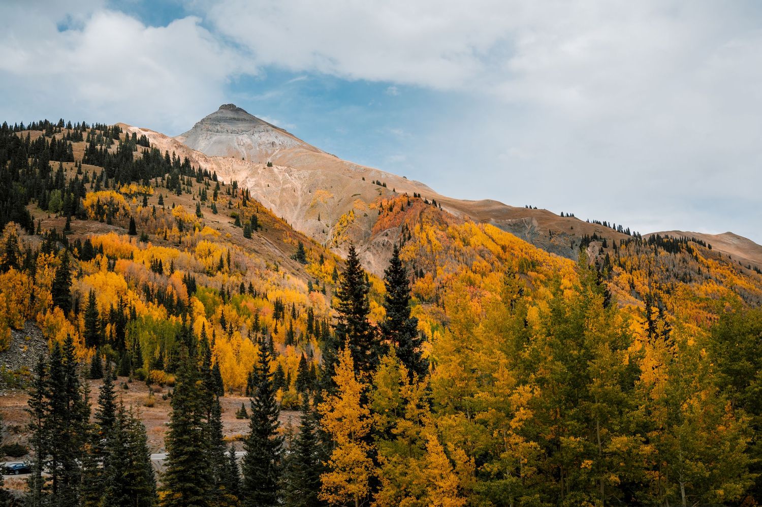 Mountain peak surrounded by golden aspen trees and evergreens in autumn.