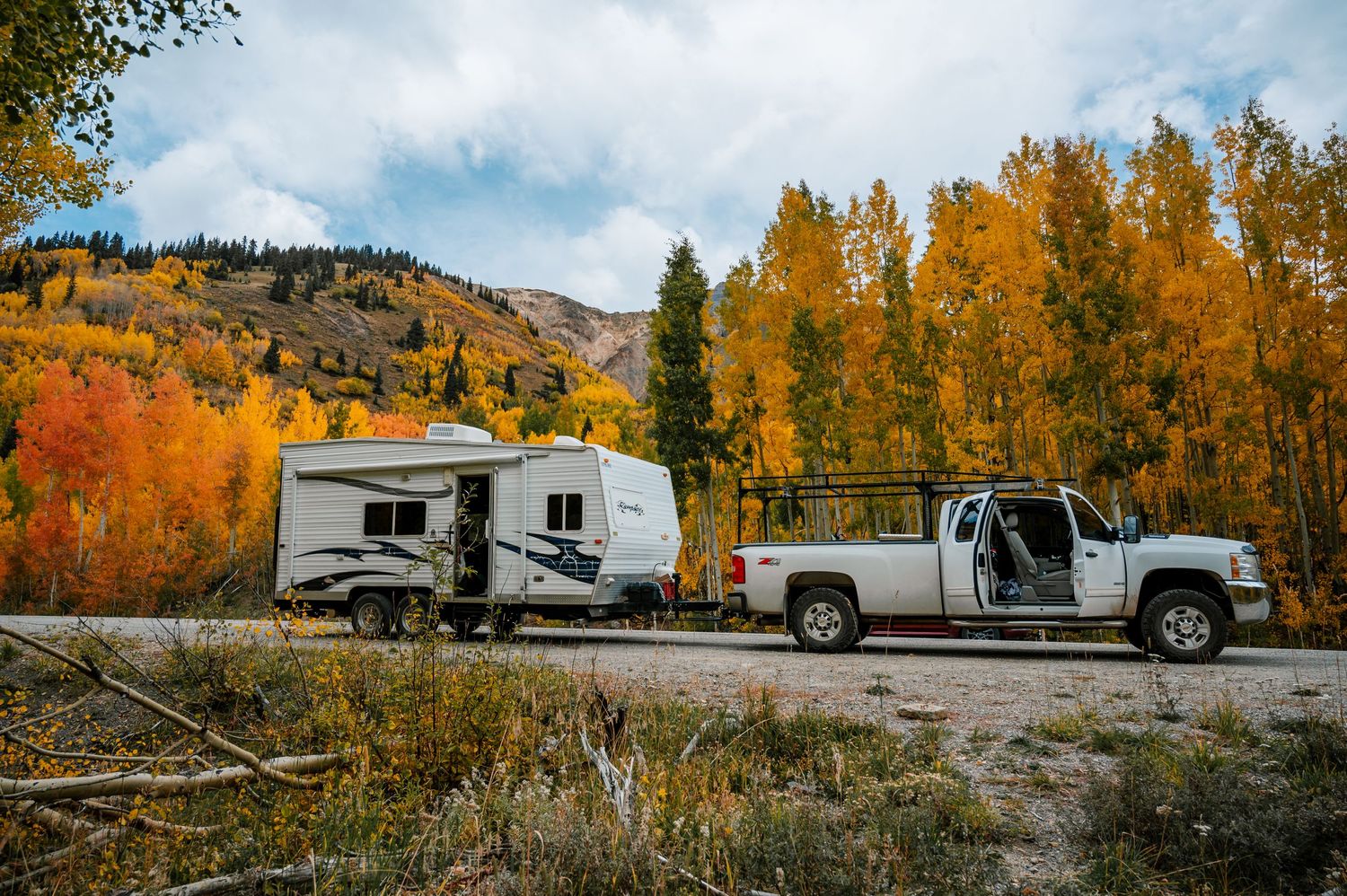 RV and truck parked along a scenic mountain road surrounded by vibrant fall colors.
