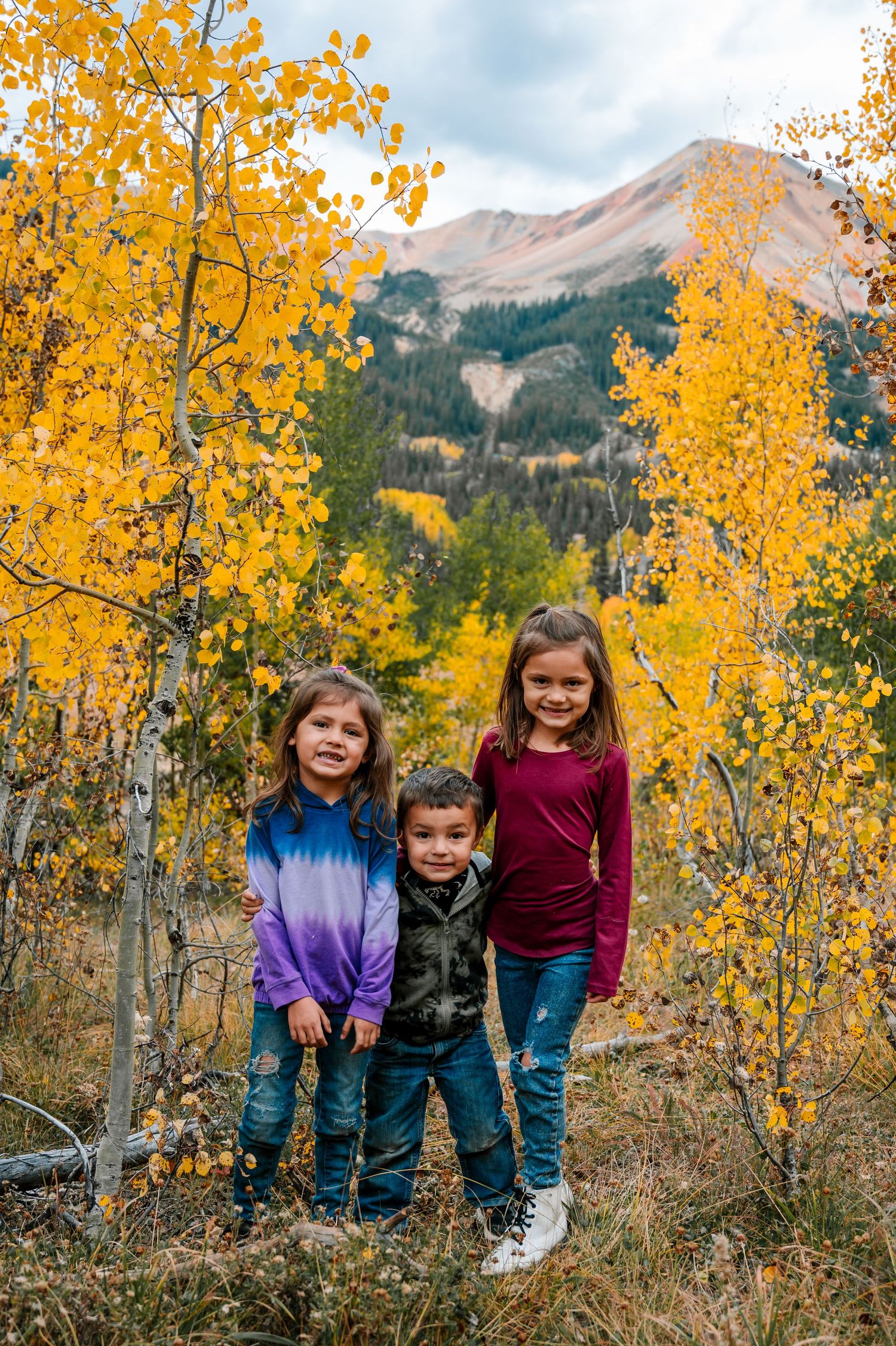 Group enjoying autumn scenery among golden aspen trees with mountain backdrop.