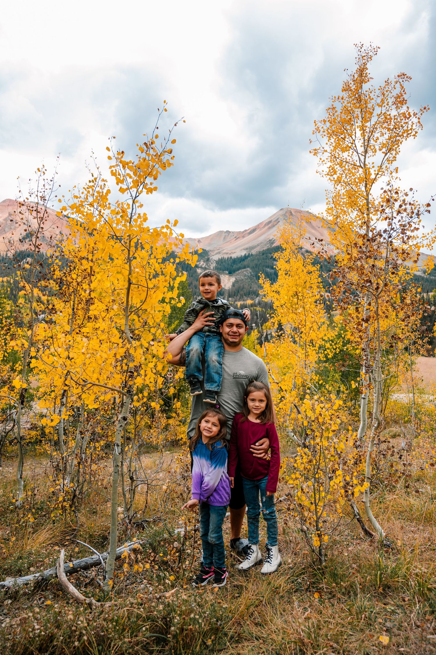 Family photo amongst golden aspen trees with mountain vista in background.