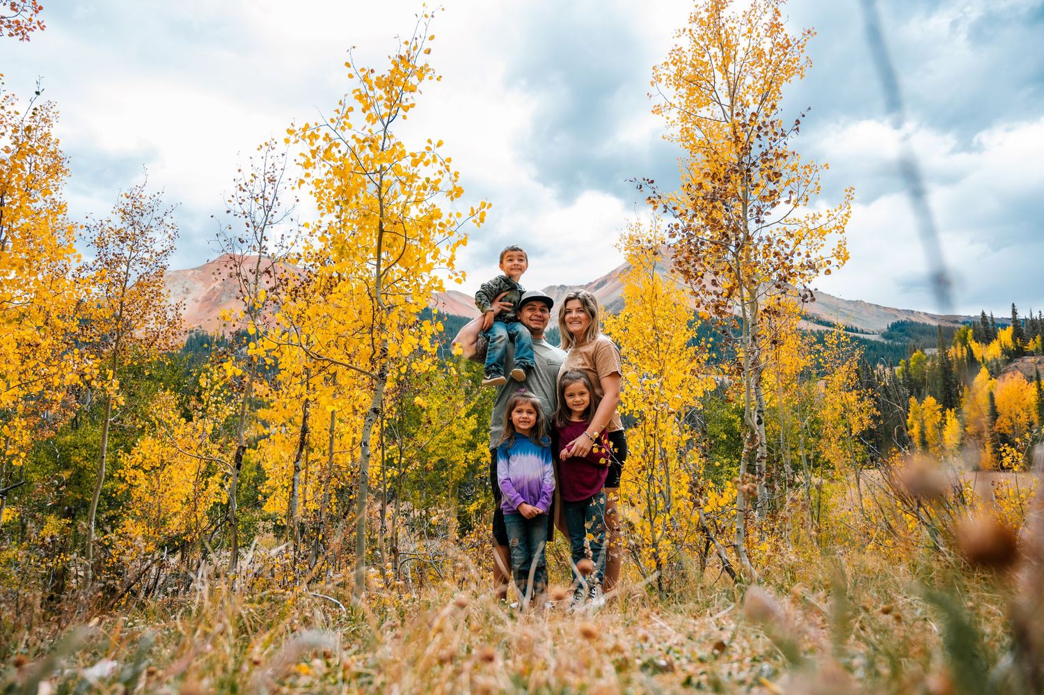 Golden aspen trees line a mountainside trail during fall with dramatic cloudy skies above.