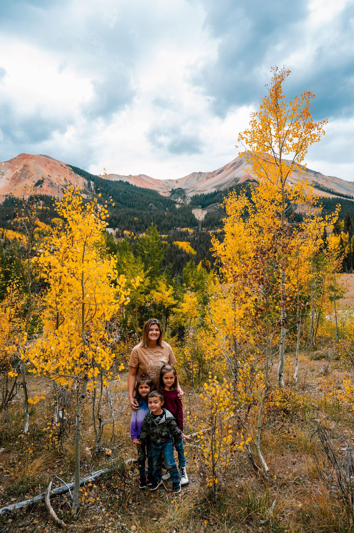 Vibrant yellow aspen trees frame mountain peaks against a cloudy blue sky in autumn.