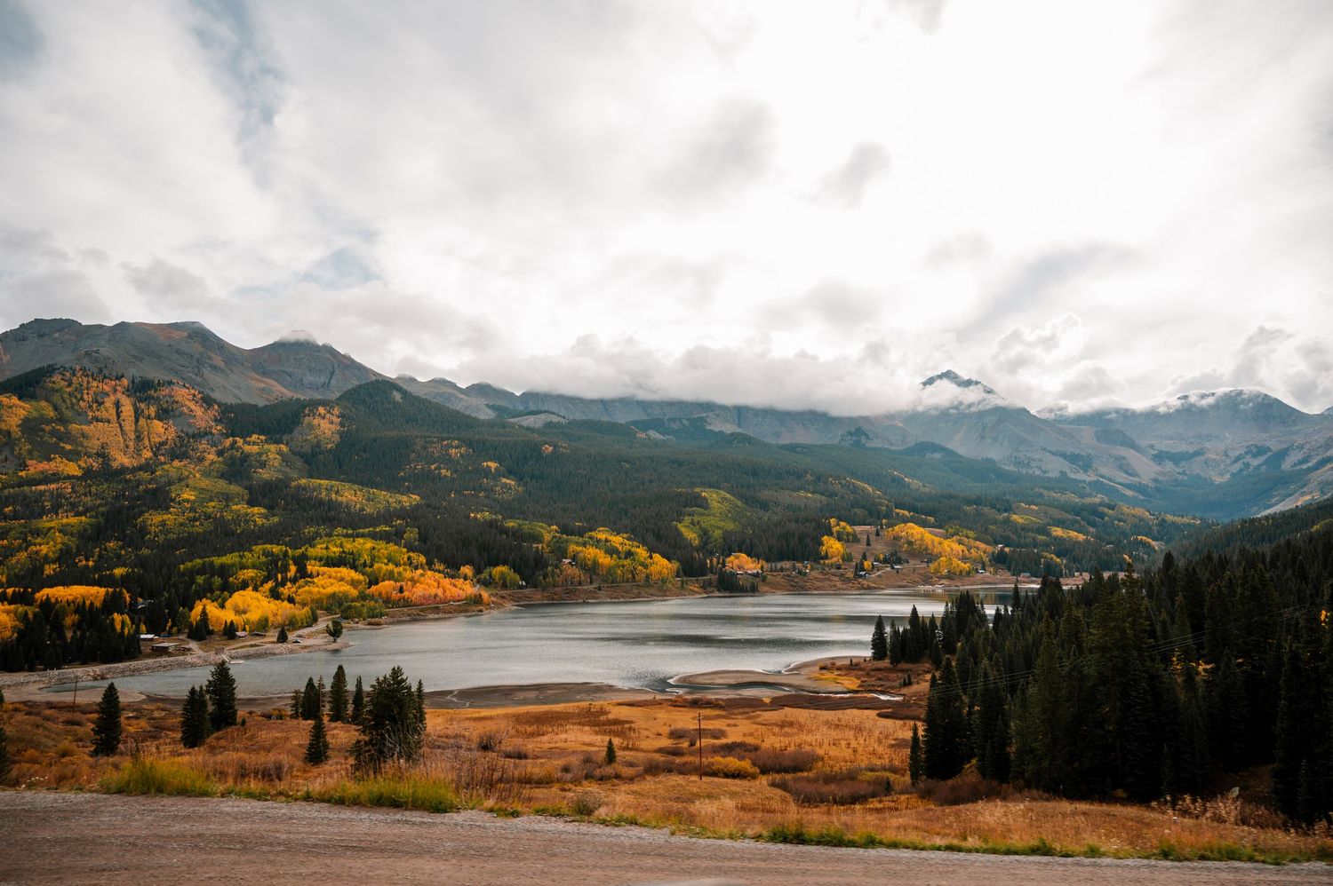 Panoramic mountain landscape with golden fall foliage and a lake in the distance.