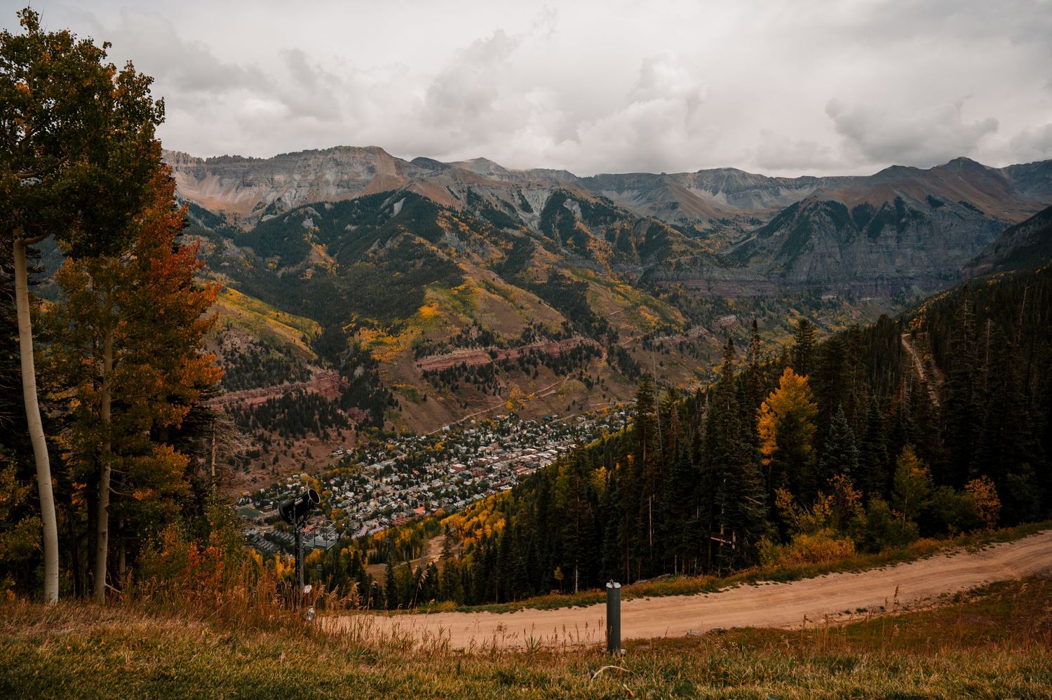 Panoramic mountain vista with rocky peaks and autumn foliage under cloudy skies.