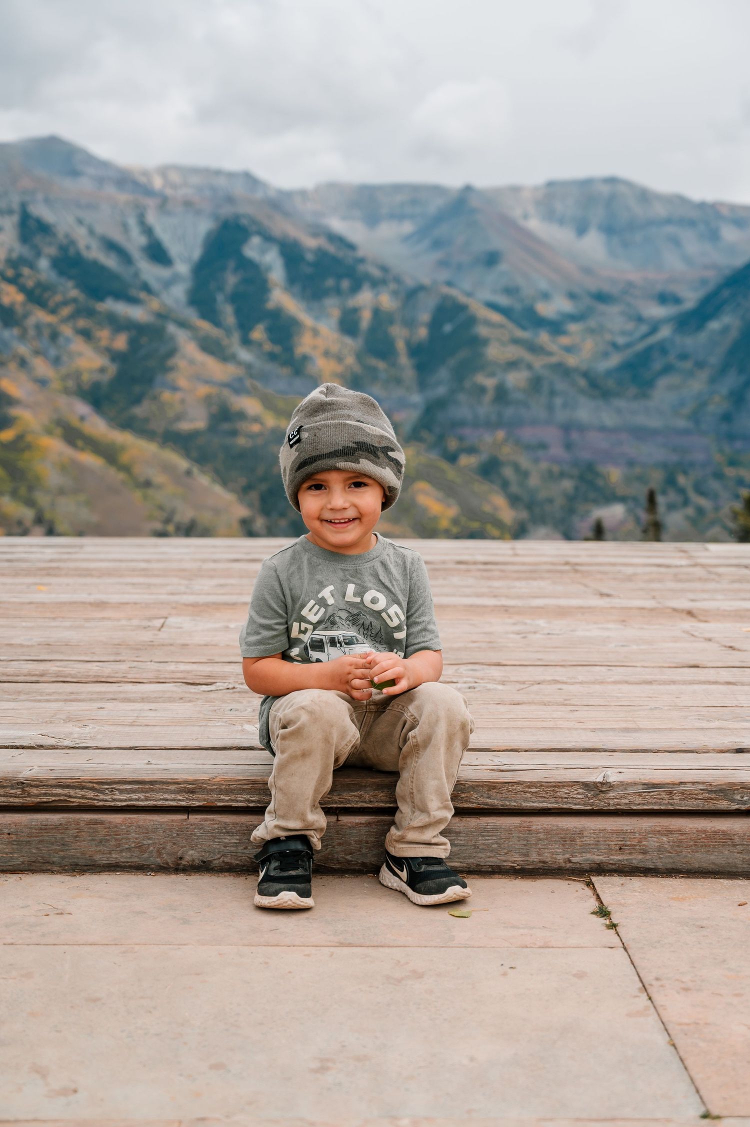A child sits on a wooden deck with stunning mountain views in the background.