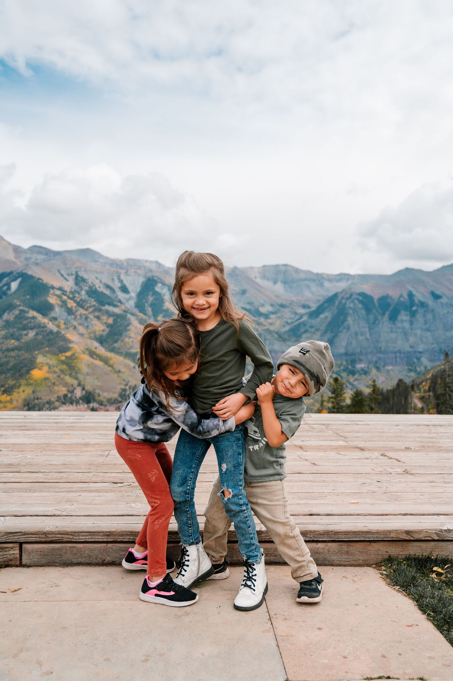 Children playing and laughing together on a wooden platform with mountain scenery.