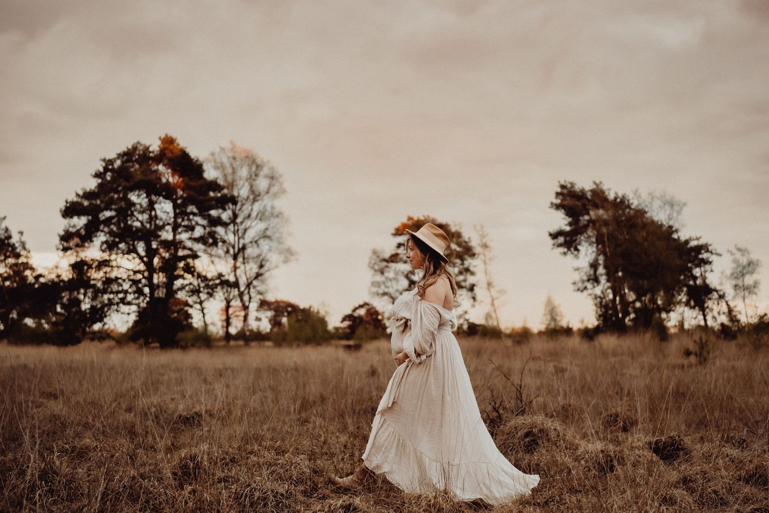 A person in a flowing white dress stands in a golden field during sunset.