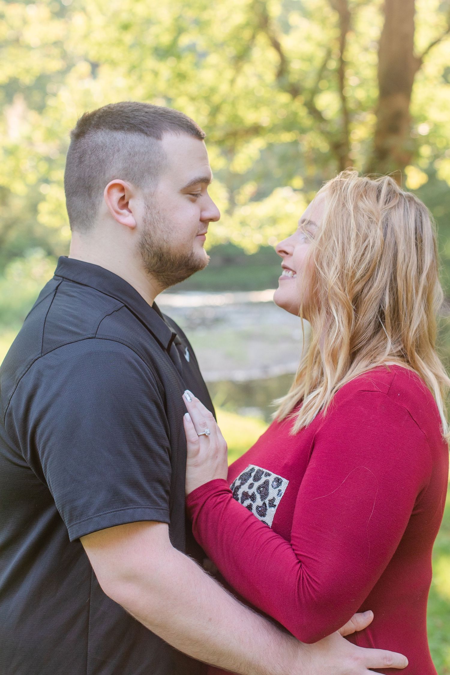 Tender moment between couple wearing red and black during outdoor engagement session.