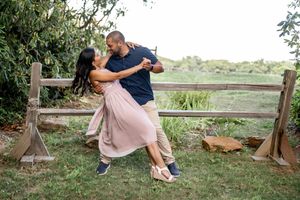 Playful engagement photo of couple dancing by rustic wooden fence.