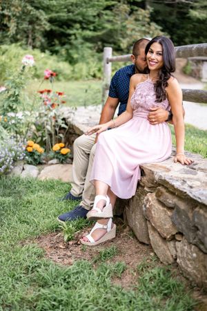A couple shares an intimate moment sitting on stone steps amid a garden with colorful flowers.