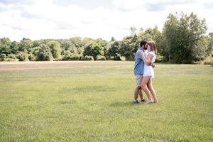 A couple embracing in a sunny meadow with trees in the background.